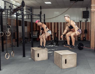 Sportif kadınlar spor salonunda birlikte atlıyor. Eğitim sınıfı sağlık kulübünde tahta kutuların üzerine atlıyor..