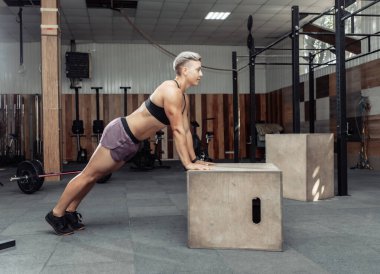 Spor salonunda tahta kutuyla şınav çeken atletik bir kadın. Cross, fonksiyonel eğitim. Sağlıklı yaşam tarzı