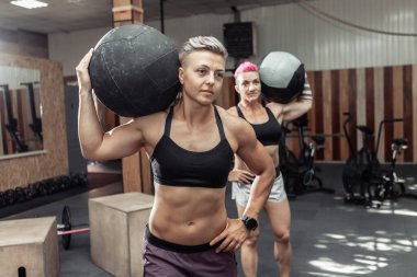 Kaslı atletik kadınlar modern bir spor salonunda ilaç toplarıyla antrenman yapıyorlar. Çapraz formda, işlevsel eğitim