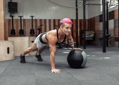 Modern bir spor salonunda kaslı atletik kadın tıp toplarıyla şınav çekiyor. Çapraz formda, işlevsel eğitim