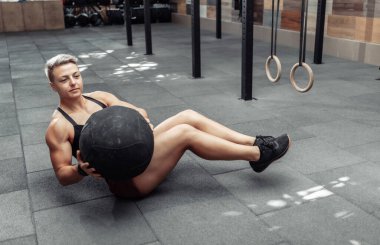 Atletik kadın modern spor salonunda karın kaslarını ilaç topuyla çalıştırıyor..