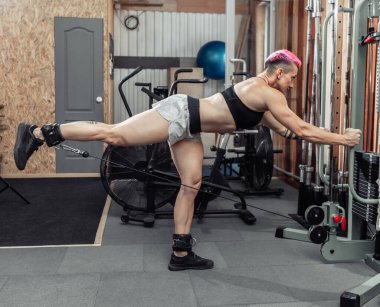 Kaslı vücut geliştiren kadın bacak kaslarını çapraz kablo makinesinde çalıştırıyor. Fitness konsepti