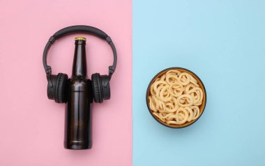 Müzik seti kulaklıklı bira şişesi, pembe mavi arka planda atıştırmalık kasesi. Üst görünüm