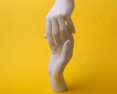 Mankenin beyaz elleri sarı arka planda birbirine dokunur. Minimalizm. Sanat kavramı