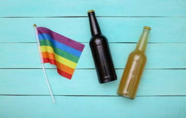 LGBT gökkuşağı bayrağı ve mavi ahşap arka planda iki şişe bira. Üst görünüm