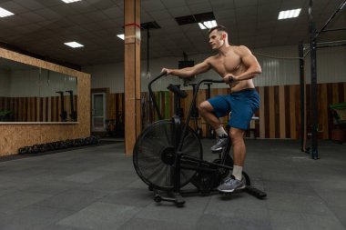 Modern bir spor salonunda çıplak gövdeli, hava motorlu güçlü bir erkek sporcu. İşlevsel, çapraz-uyum eğitimi. Kardiyo egzersizi. Sağlıklı yaşam tarzı kavramı