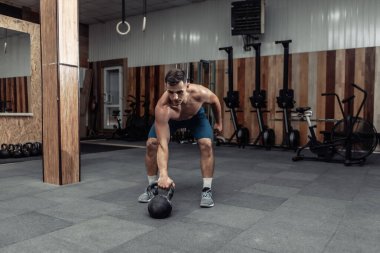 Güçlü kaslı bir adam spor salonunda ağır bir kettlebell ile egzersiz yapıyor. Serbest ağırlık ile fonksiyonel eğitim