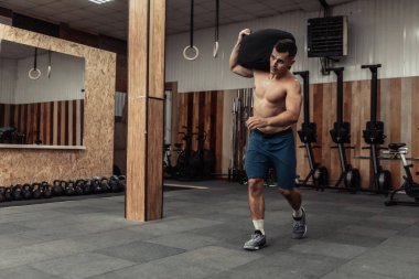 Modern çapraz spor salonunda kaslı erkek sporcu ağır torbayla egzersiz yapıyor. Fonksiyonel eğitim