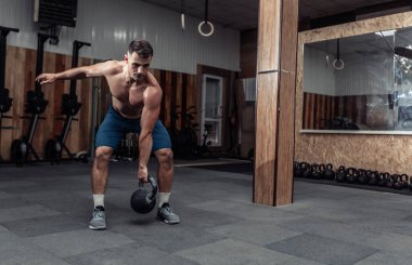 Güçlü kaslı bir adam spor salonunda ağır bir kettlebell ile egzersiz yapıyor. Serbest ağırlık ile fonksiyonel eğitim