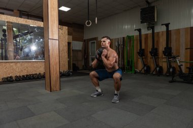 Güçlü kaslı bir adam spor salonunda ağır bir kettlebell ile egzersiz yapıyor. Serbest ağırlık ile fonksiyonel eğitim