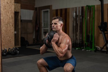 Güçlü kaslı bir adam spor salonunda ağır bir kettlebell ile egzersiz yapıyor. Serbest ağırlık ile fonksiyonel eğitim