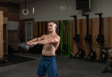 Güçlü kaslı bir adam spor salonunda ağır bir kettlebell ile egzersiz yapıyor. Serbest ağırlık ile fonksiyonel eğitim