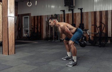 Güçlü kaslı bir adam spor salonunda ağır bir kettlebell ile egzersiz yapıyor. Serbest ağırlık ile fonksiyonel eğitim