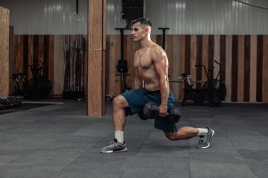 Bacaklarını çalıştıran kaslı bir adam modern spor salonunda ağır dambıllarla hareket ediyor. Sağlıklı yaşam tarzı kavramı