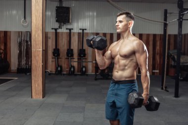 Kaslı adam ağır dambıllarla egzersiz yapıyor, spor salonunda kaslarını çalıştırıyor. Sağlıklı yaşam tarzı