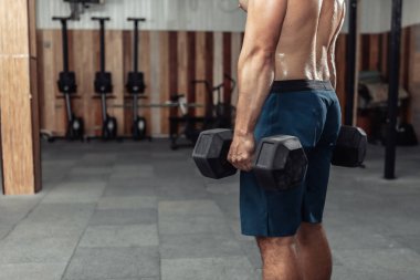 Spor salonunda ağır dambıllar tutan kaslı bir adam.