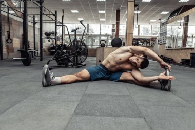 Genç kaslı adam modern sağlık kulübünde kas esneme hareketleri yapıyor.