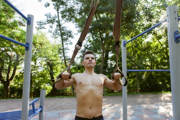 年轻英俊的男子赤身裸体的躯干在室外运动场上训练与桁架阻力系统 健康生活方式概念 — 图库照片