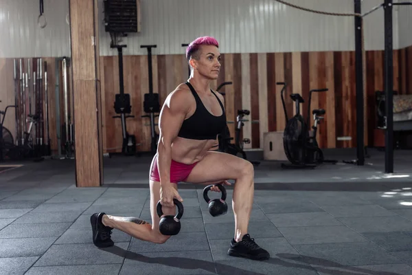 肌肉发达的女运动员 一头粉色的短发 带着沉重的水壶突起 现代体育馆的功能性交叉训练 — 图库照片