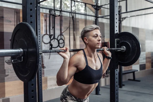 一个年轻的肌肉发达的女运动员的画像 她的肩膀上挂着一个杠铃 在一个现代的交叉体育馆里 健身概念 — 图库照片