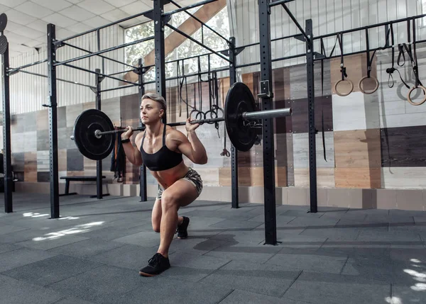 Athletic woman doing lunges exercise with barbell on shoulders in modern gym