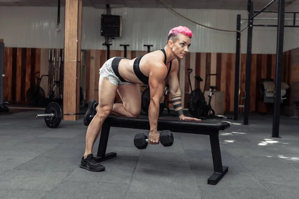 Atletik kadın tek eliyle dambıl sırığı egzersizi yapıyor. Sırt kası eğitimi. Vücut geliştirme ve Fitness