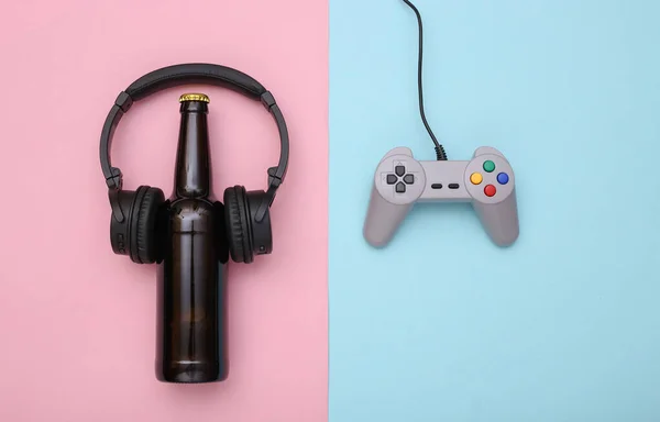 娯楽の時間だ ピンクブルーのパステルカラーの背景にヘッドフォンでゲームパッドとビールボトル トップ表示 — ストック写真