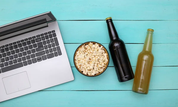 Rest time. Laptop, bottle of beer and popcorn bowl on a blue wooden background. Top view