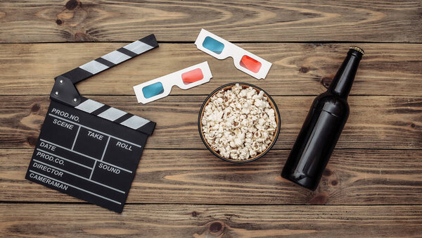 Movie time. Movie clapperboard, 3d glasses, bottle of beer, popcorn on wooden background. Top view