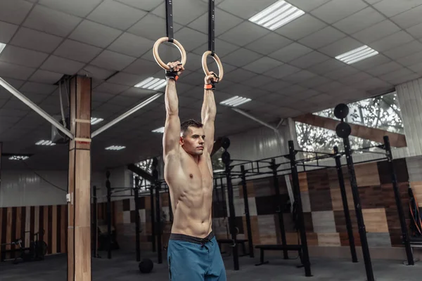 Muscular male gymnast exercising on gymnastic rings in a modern health club. Healthy lifestyle concept