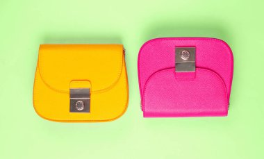 Yeşil arka planda pembe ve sarı deri mini çantalar. Minimalizm moda kavramı. Üst görünüm
