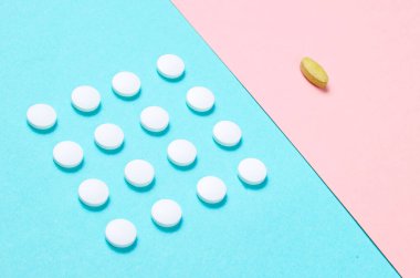 Asgari tıbbi konsept. Bir grup özdeş beyaz tablet ve pastel renkli arka plan üzerinde eşsiz bir tablet. Üst görünüm