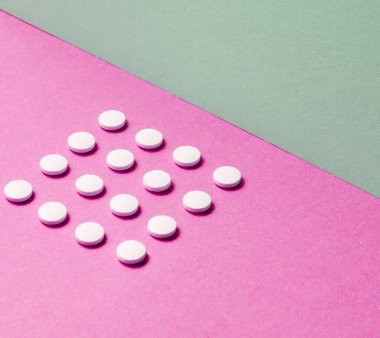 Asgari tıbbi konsept. Pastel renkli arka planda aynı beyaz tabletlerden oluşan bir grup. Üst görünüm