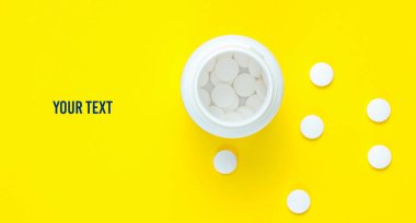 Asgari tıbbi konsept. Sarı pastel arka planda beyaz haplarla dolu açık bir şişe. Uzayı kopyala Üst görünüm