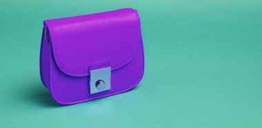 Mavi arka planda metal kilidi olan mor deri bir çanta..