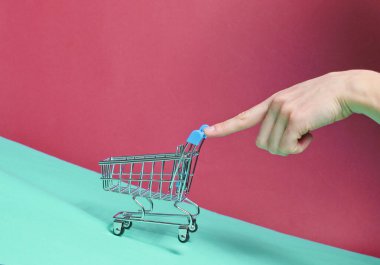 Kadın parmağı eğimli, küçük, boş bir alışveriş arabası itiyor. Alışveriş konsepti, teslimat