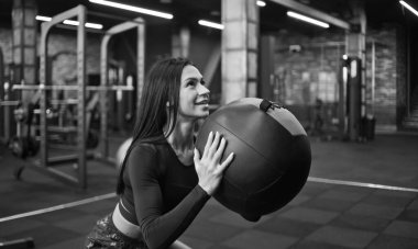 Spor kıyafetli neşeli esmer kadın ilaç topuyla egzersiz yapıyor..