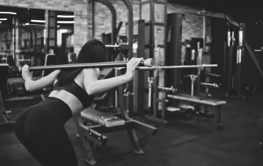 Sıska esmer sporcu, spor salonunda vücudunu eğerek omuzlarındaki çıtçıtla jimnastik yapıyor. Arka plan