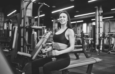 Gülümseyen genç bir kadın spor salonunda bir bankta otururken el ele tutuşur.