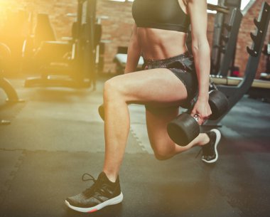 Spor salonunda elinde dambıllarla egzersiz yapan formda bir kız.