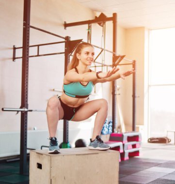 İşlevsel modern eğitim. Genç sarışın bir kadın uzun tahta bir kutunun üzerine çömeldi..