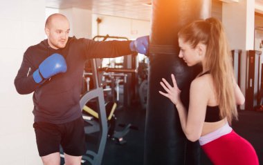 Kadın eğitmen kum torbasını tutuyor ve bir boksörü eğitiyor. Genç çift eğitimi