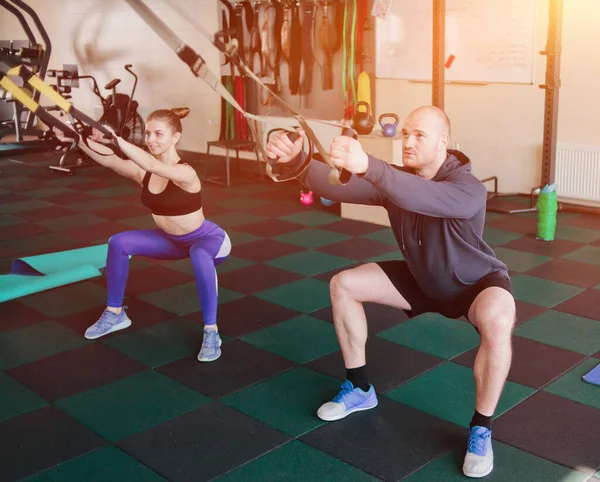 Couple functional training. Woman and man doing exercise with fitness straps at gym.