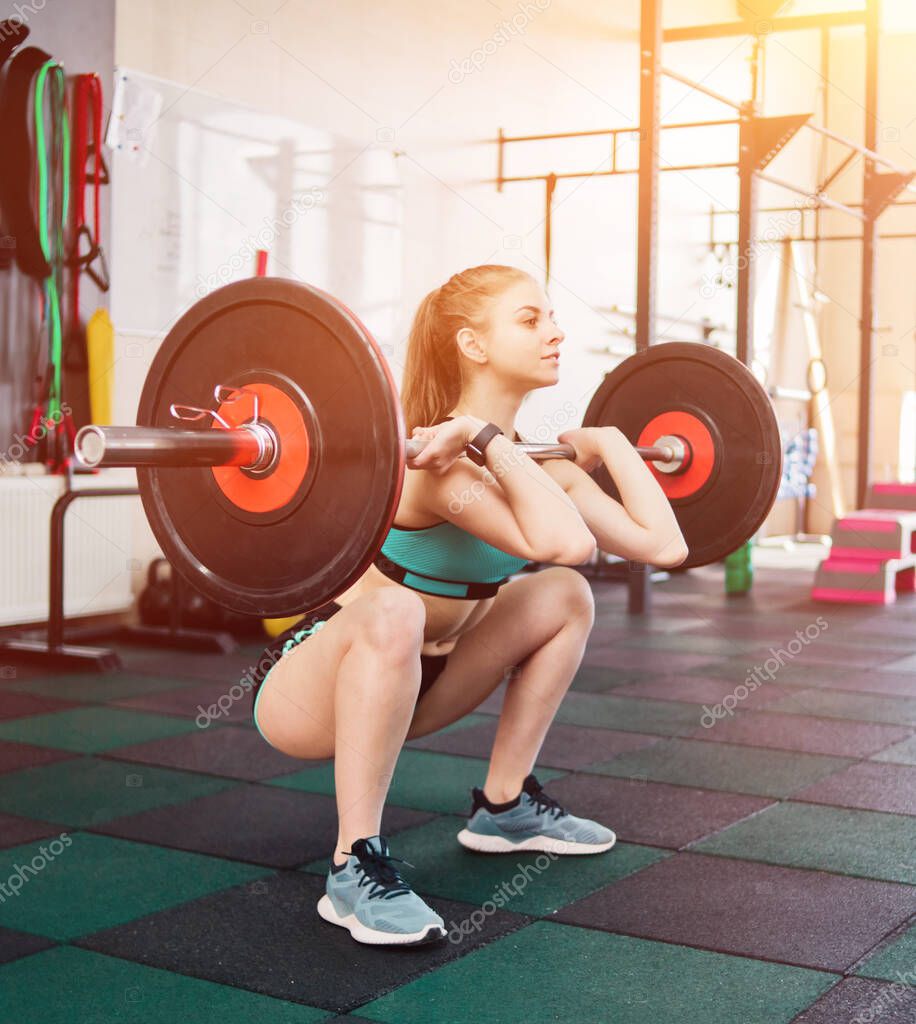 Young athlete woman in sportswear doing front squats with a barbell on the chest in the gym