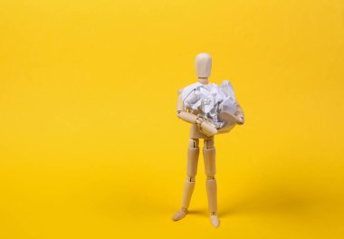 Sarı arka planda buruşmuş kağıt yumağı tutan tahta kukla.
