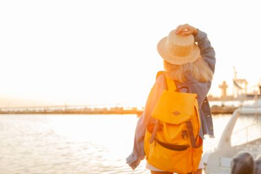 Gündoğumunda denizde büyük bir sırt çantasıyla gezen genç bir turist. Seyahat ve turizm kavramı