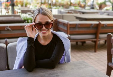 Açık kafedeki masada oturan şık bir bayanın portresi.