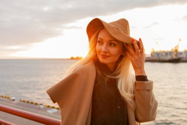 Güneşin doğuşunda keçeli şapkalı ve ceketli şık sarışın kadın.