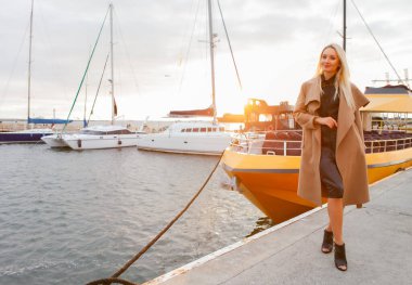 Gündoğumunda bir yat kulübünde poz veren güler yüzlü genç bir kadının portresi.