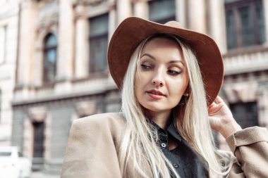 Sonbahar montu ve şehir mimarisi arka planında şapkası olan şık bir kadının dramatik portresi.